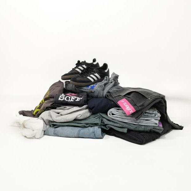 A stack of pre-loved clothing and sneakers on a white studio floor